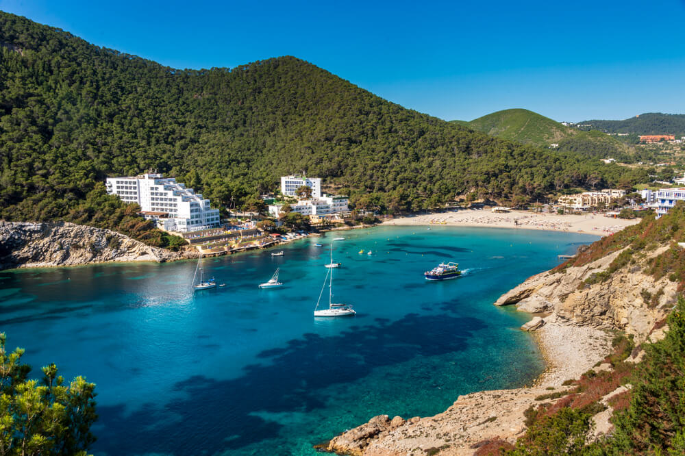 Cala Llonga, Ibiza: Spiaggia sabbiosa e porto naturale con hotel turistici.